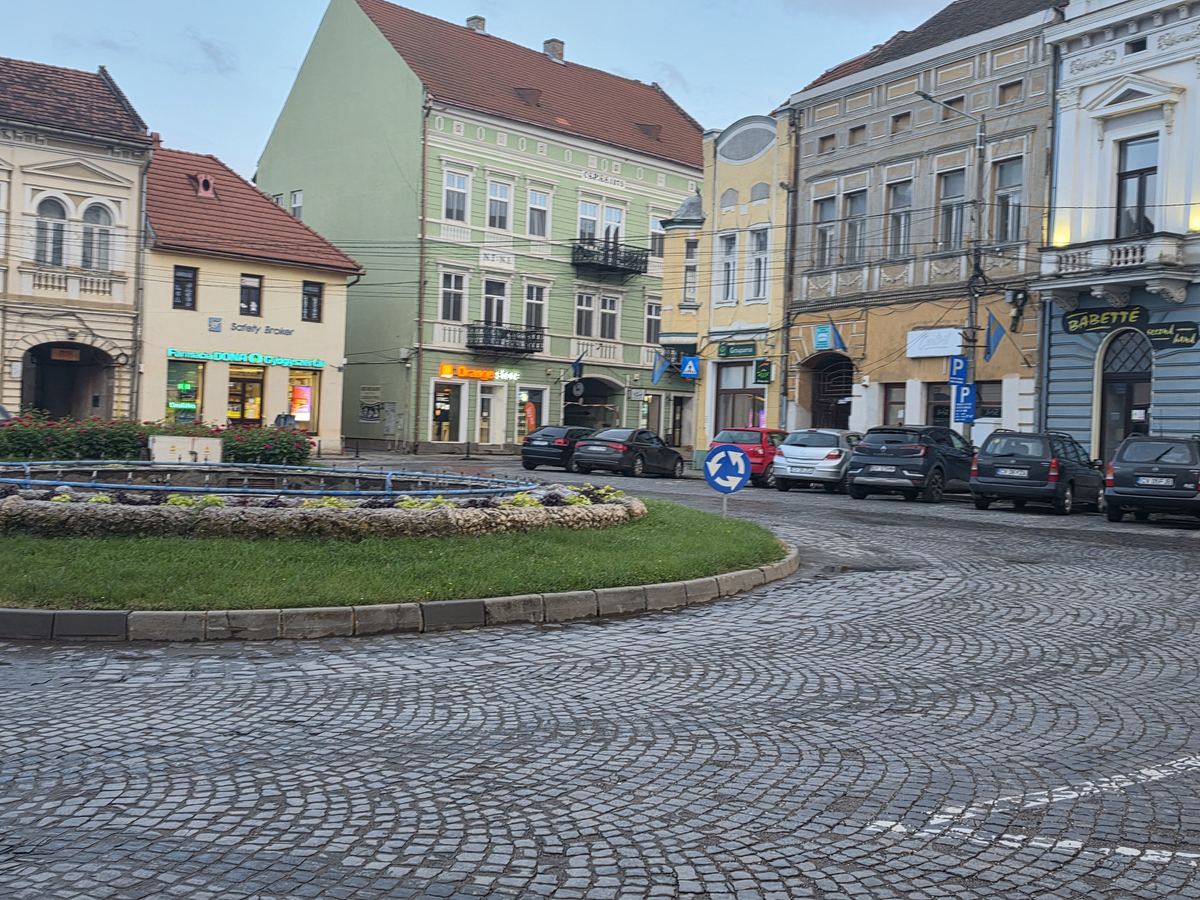 Centrul orașului Târgu Secuiesc, cu rondul de flori, magazinele și clădirile din piața centrală